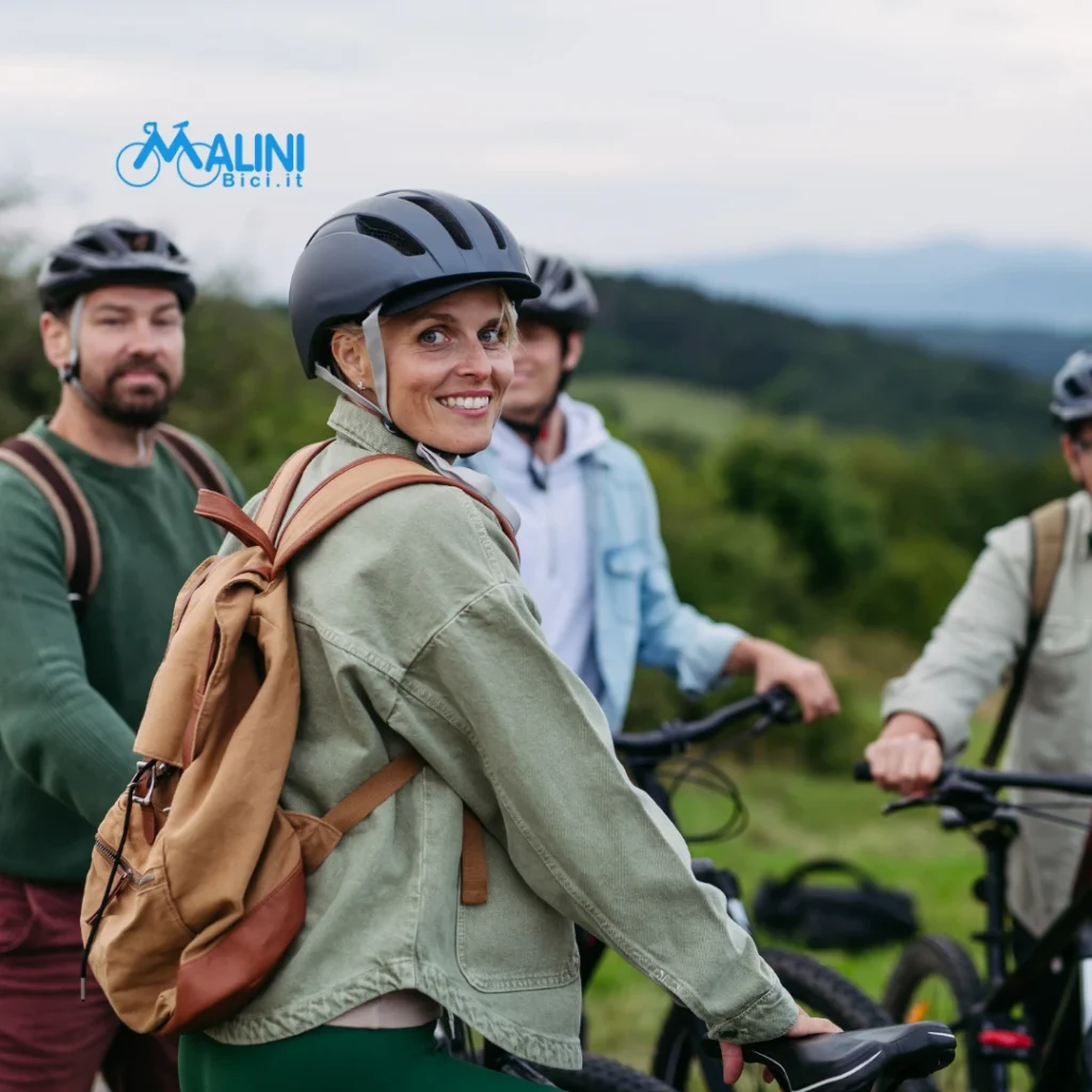 Gruppo di ciclisti con casco durante una sosta all’aperto in un paesaggio collinare e verde.