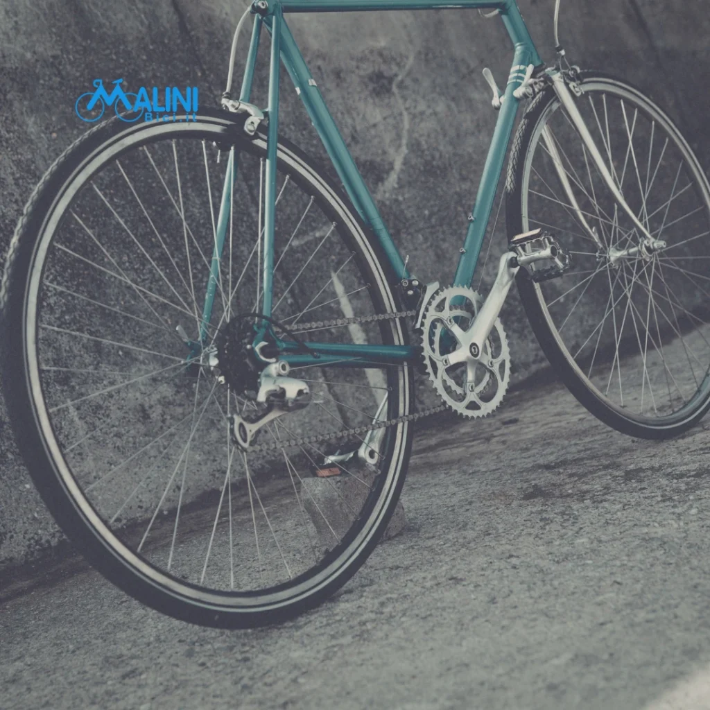 Bicicletta da strada appoggiata vicino a un muro con ruote, telaio e trasmissione ben visibili.