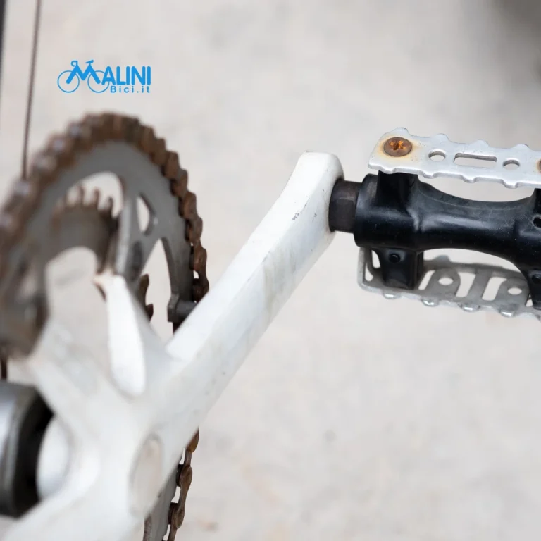Dettaglio di pedale, pedivella e corona di una bicicletta con catena in primo piano.